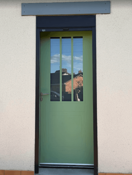 Porte d'entrée vert sauge avec trois vitres verticales et un cadre noir sur mur beige.