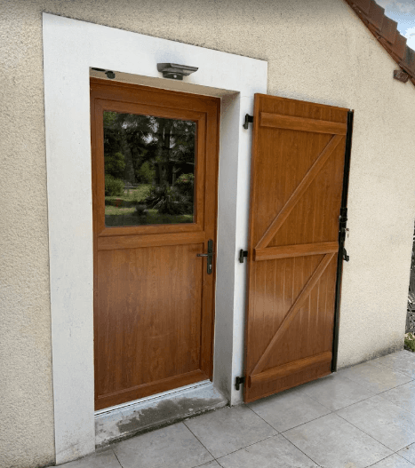 Porte d'entrée marron imitation bois avec vitre et volet battant ouvert sur mur en crépi.