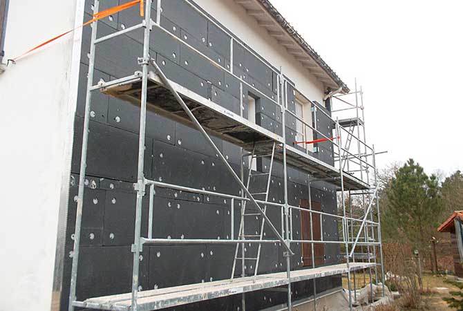 Pose de panneaux isolants noirs sur la façade d'une maison avec un échafaudage métallique.