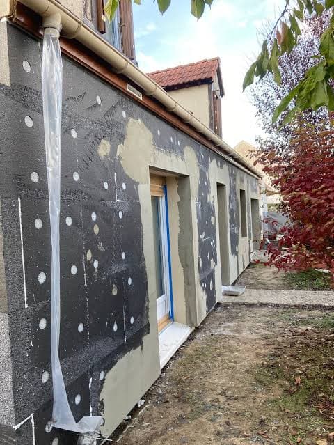 Isolation thermique extérieure d'un mur avec panneaux gris, chevilles de fixation et enduit.